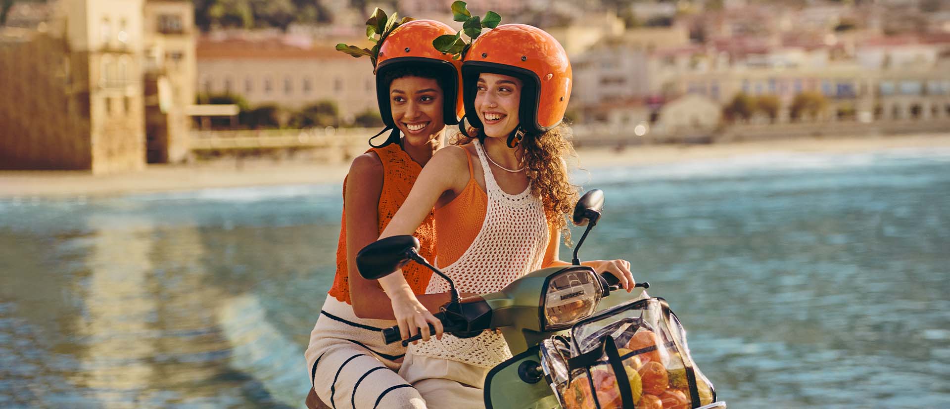 Zwei lächelnde Mädchen auf einem Motorrad mit Orangen