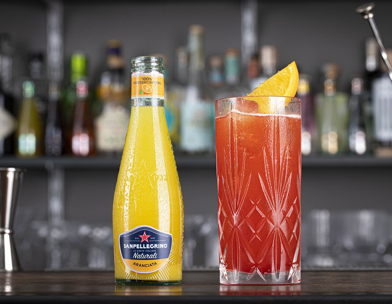 Aranciata Naturali Sanpellegrino con bicchiere di cocktail Garibaldi accanto su bancone bar