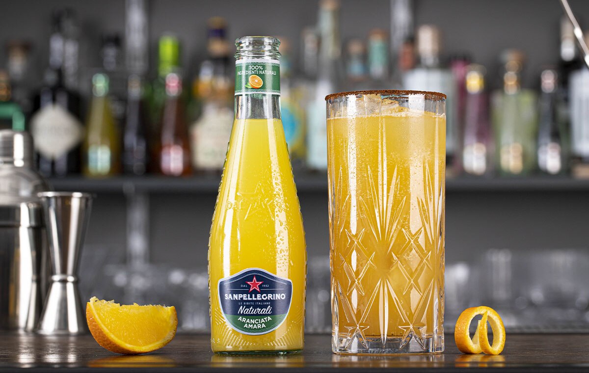 Aranciata amara Naturali Sanpellegrino con bicchiere di Crusta Richey accanto su bancone bar thumb