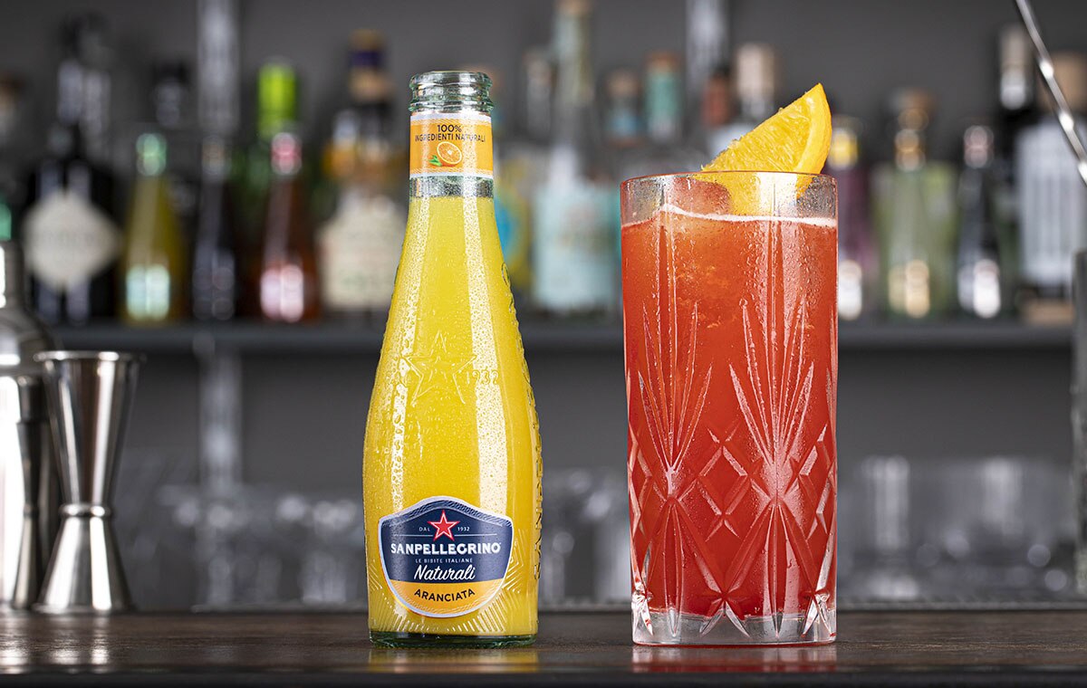 Aranciata Naturali Sanpellegrino con bicchiere di cocktail Garibaldi accanto su bancone bar-thumb