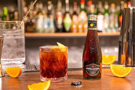 Bottiglia di Chinò Sanpellegrino con bicchiere di cocktail Americano accanto su bancone del bar Bottiglia di Chinò Sanpellegrino con bicchiere di cocktail Americano accanto su bancone del bar