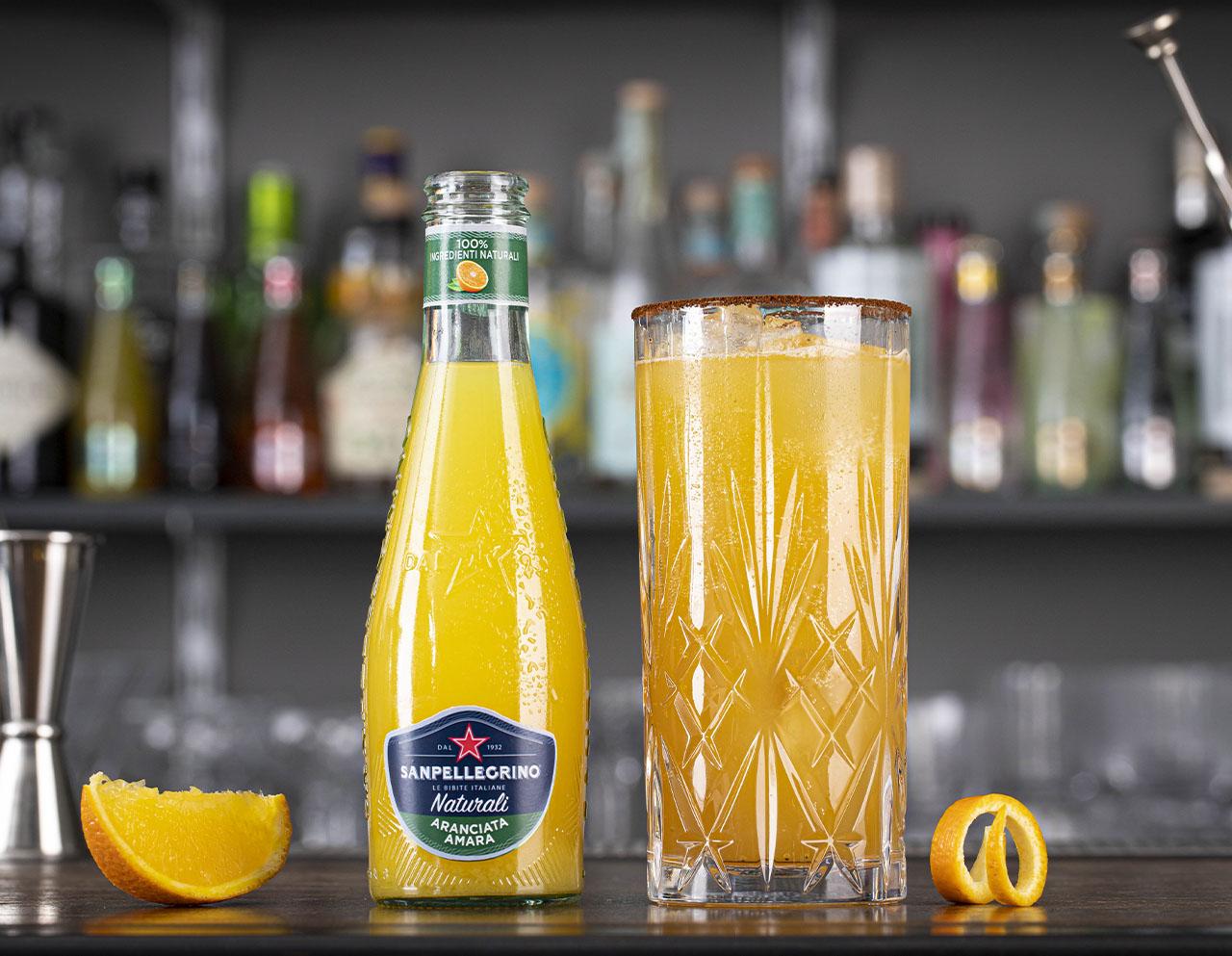 Aranciata amara Naturali Sanpellegrino con bicchiere di Crusta Richey accanto su bancone bar