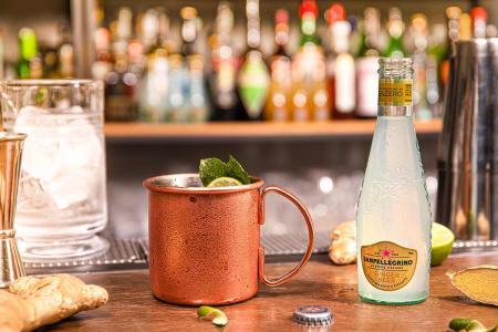 Bottiglia di Ginger Beer Sanpellegrino con tazza di Mule Profumato accanto su bancone del bar