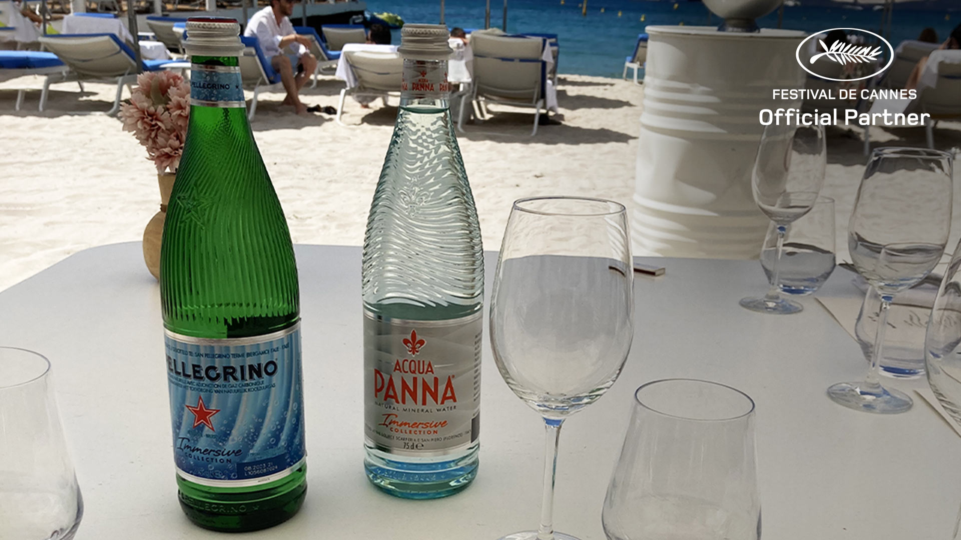 A bottle of Acqua Panna Immersive Collection next to a glass and the beach in the background