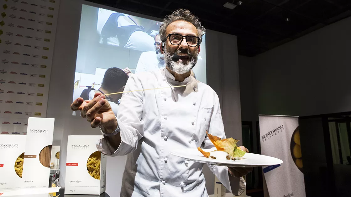 A chef holding a plate while talking on a microphone and looking at the camera