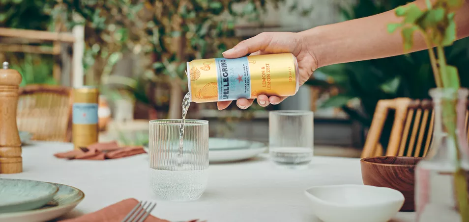 Pouring S.Pellegrino Essenza lemon sparkling water into a glass on a table