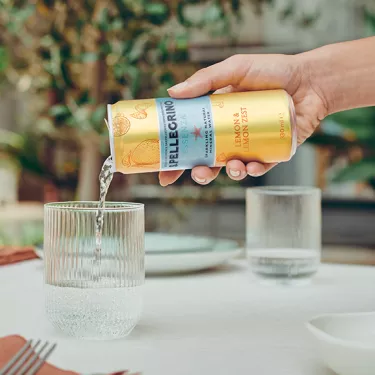 Pouring S.Pellegrino Essenza lemon sparkling water into a glass on a table