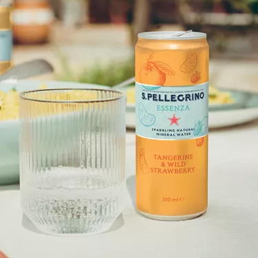 S.Pellegrino Essenza tangerine and wild strawberry can on a table with a glass