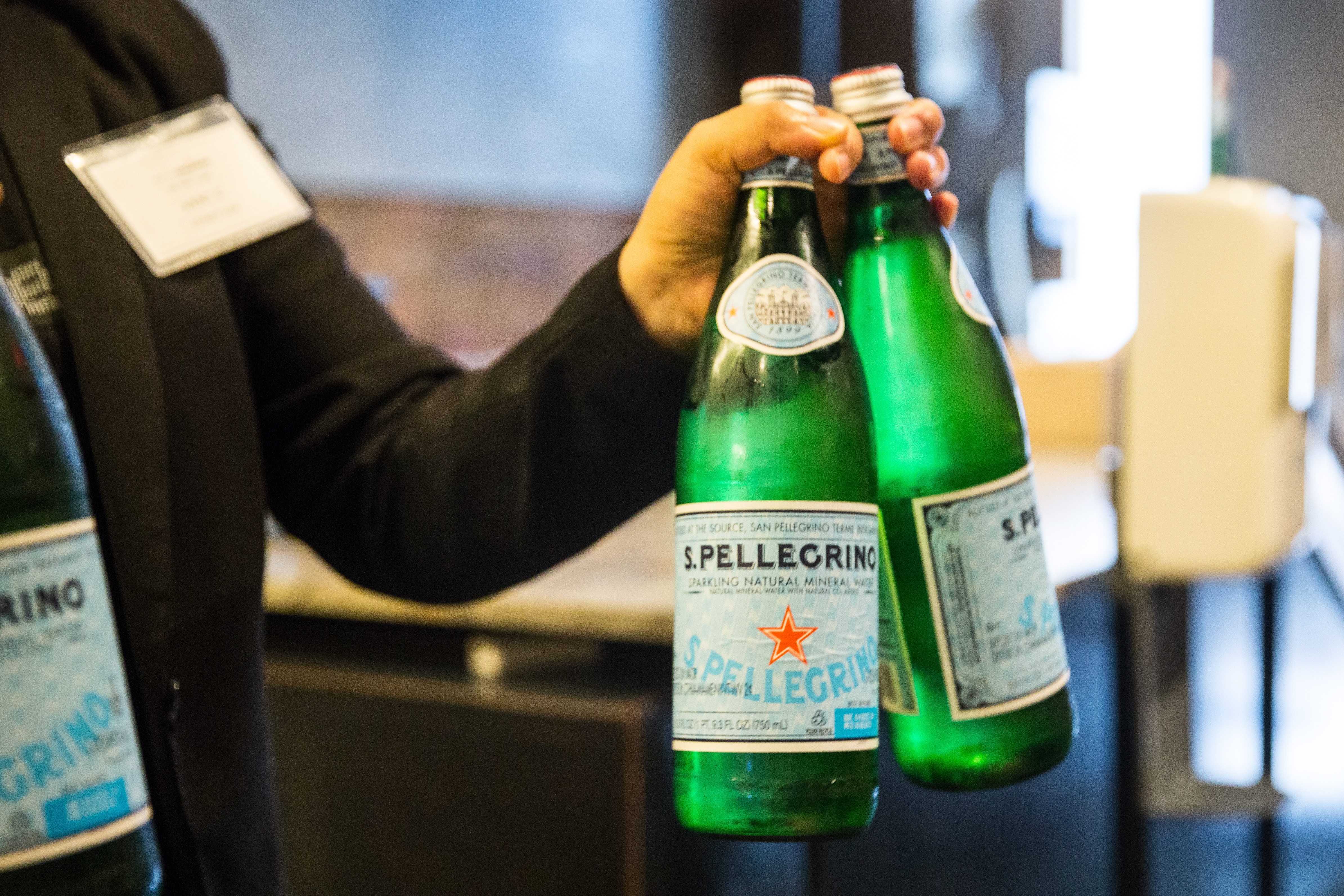 Hand holding three green bottles of San Pellegrino sparkling water with the iconic red star label.