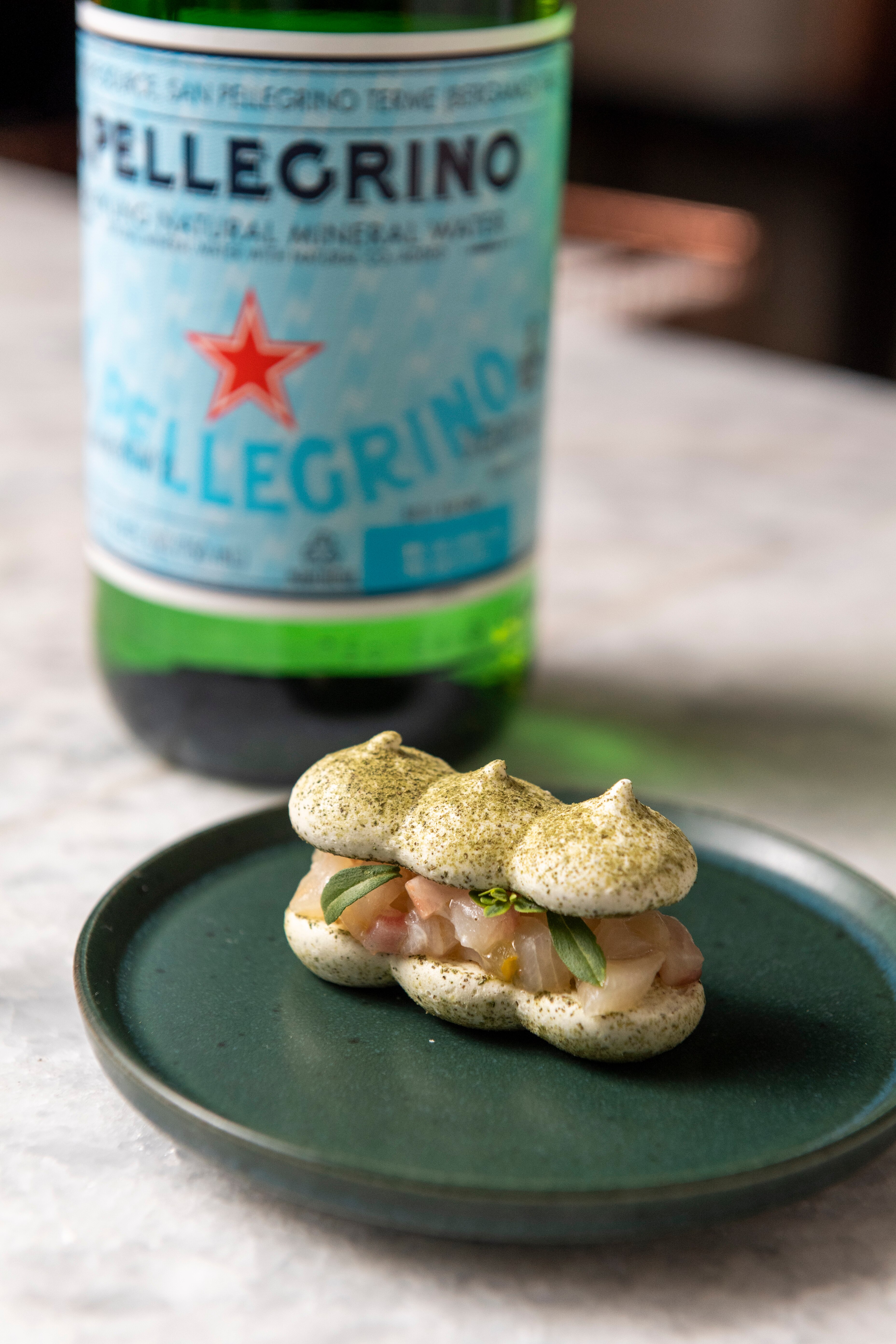 Meringue with savory filling on a green plate in front of a San Pellegrino bottle.