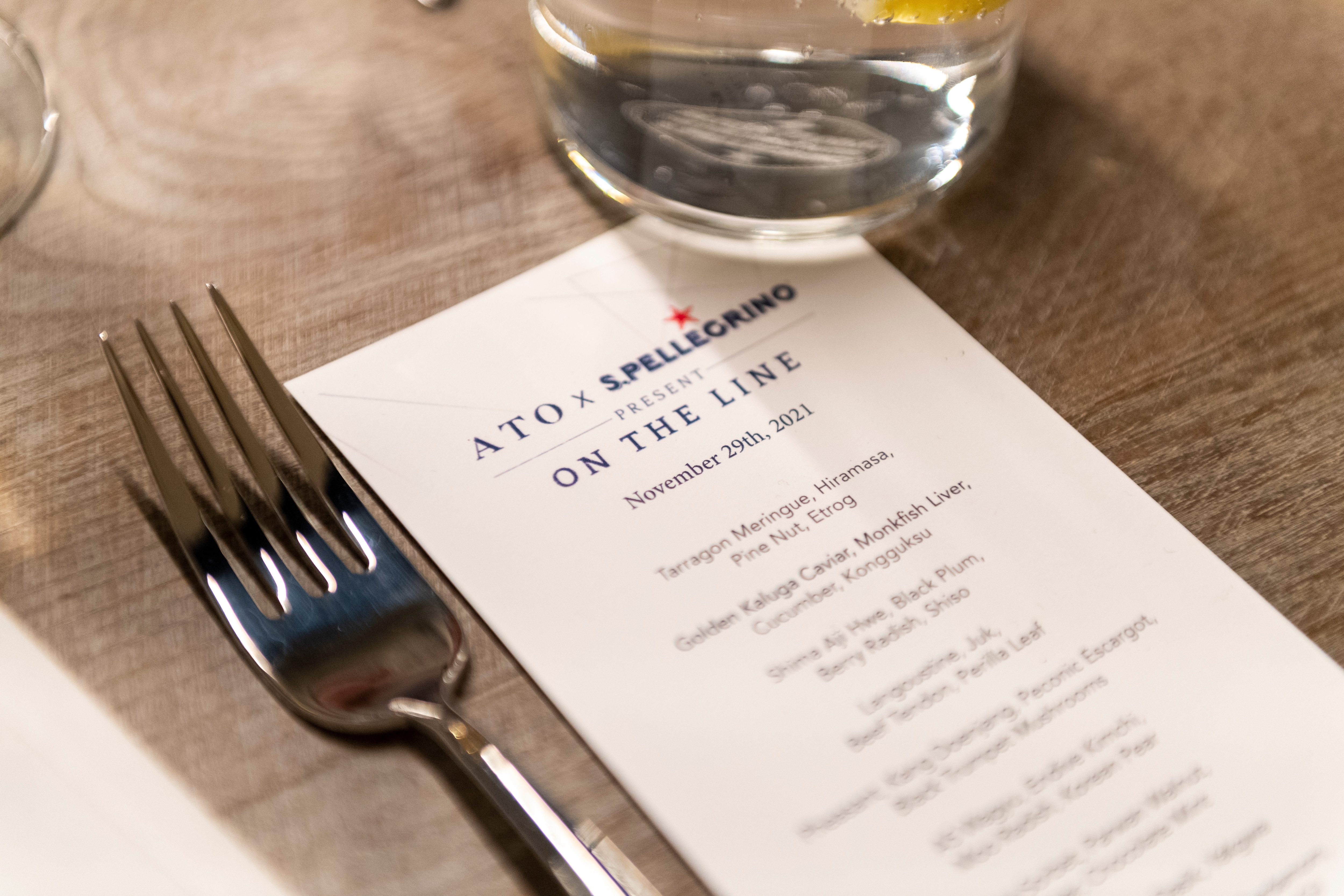 Menu for &quot;ATO x S.Pellegrino&quot; event, November 29, 2021, with a fork on a wooden table.