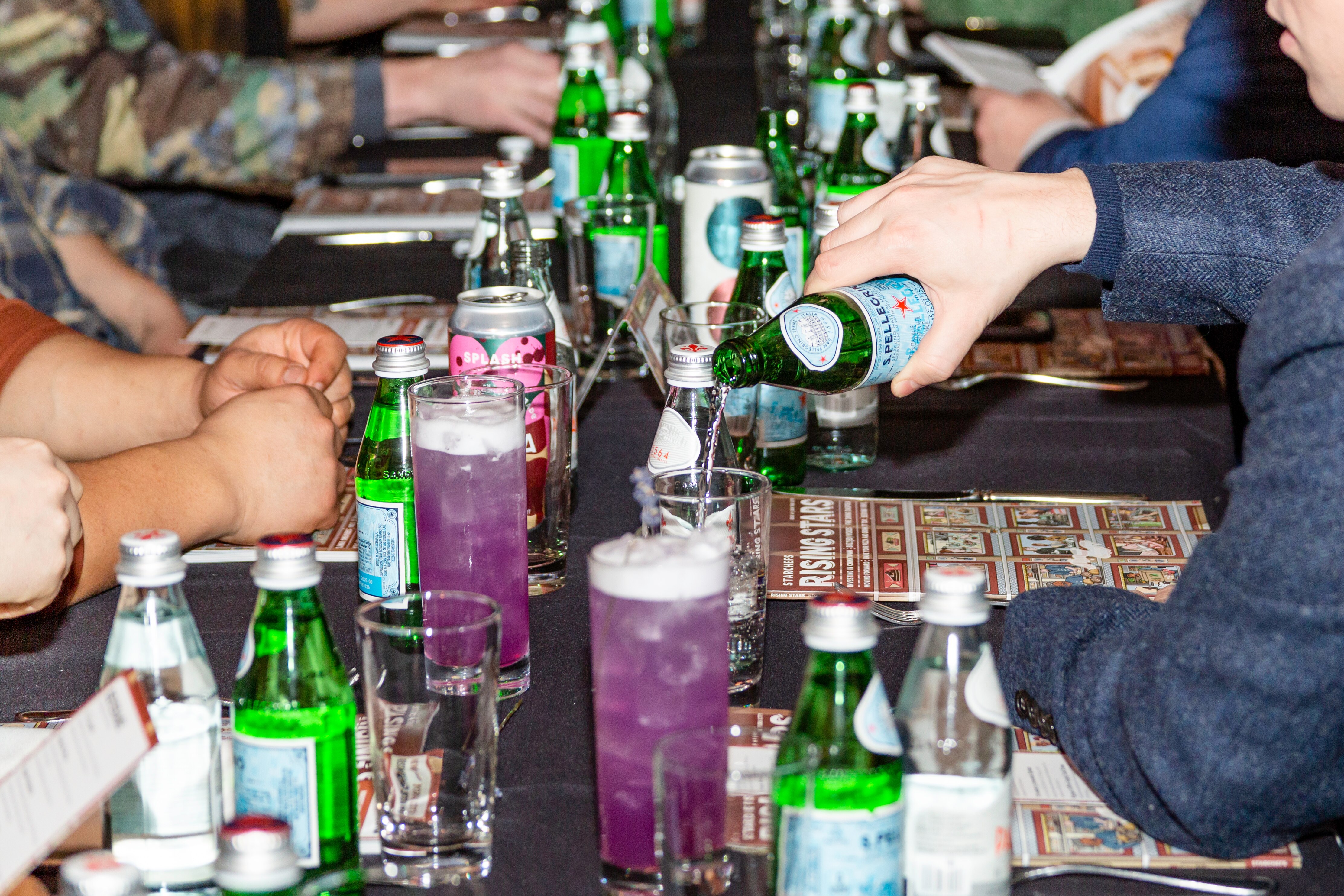 A person pouring S.Pellegrino into a glass at a Rising Stars event dinner.
