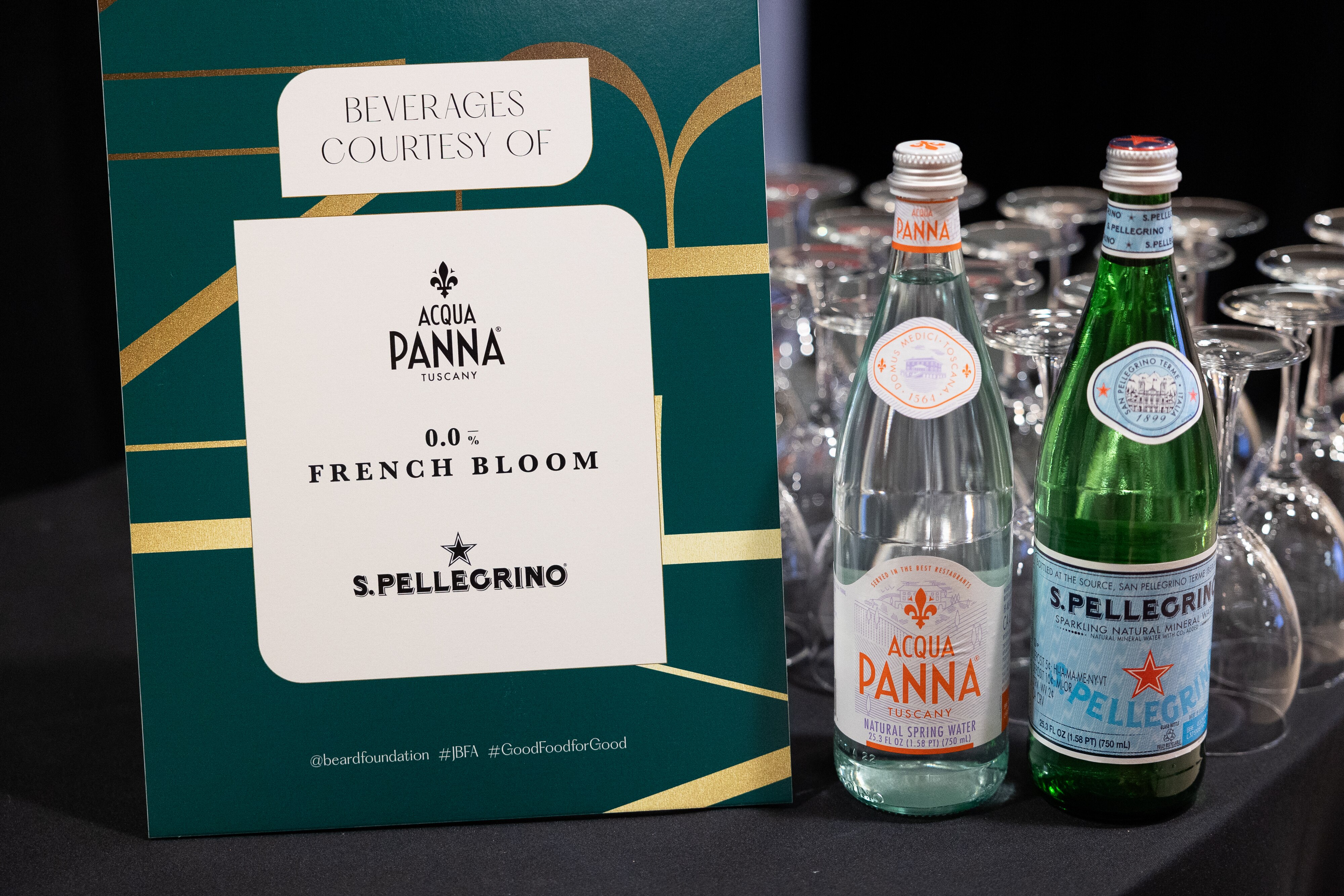 Acqua Panna and San Pellegrino bottles next to a sign listing event beverages, with wine glasses.