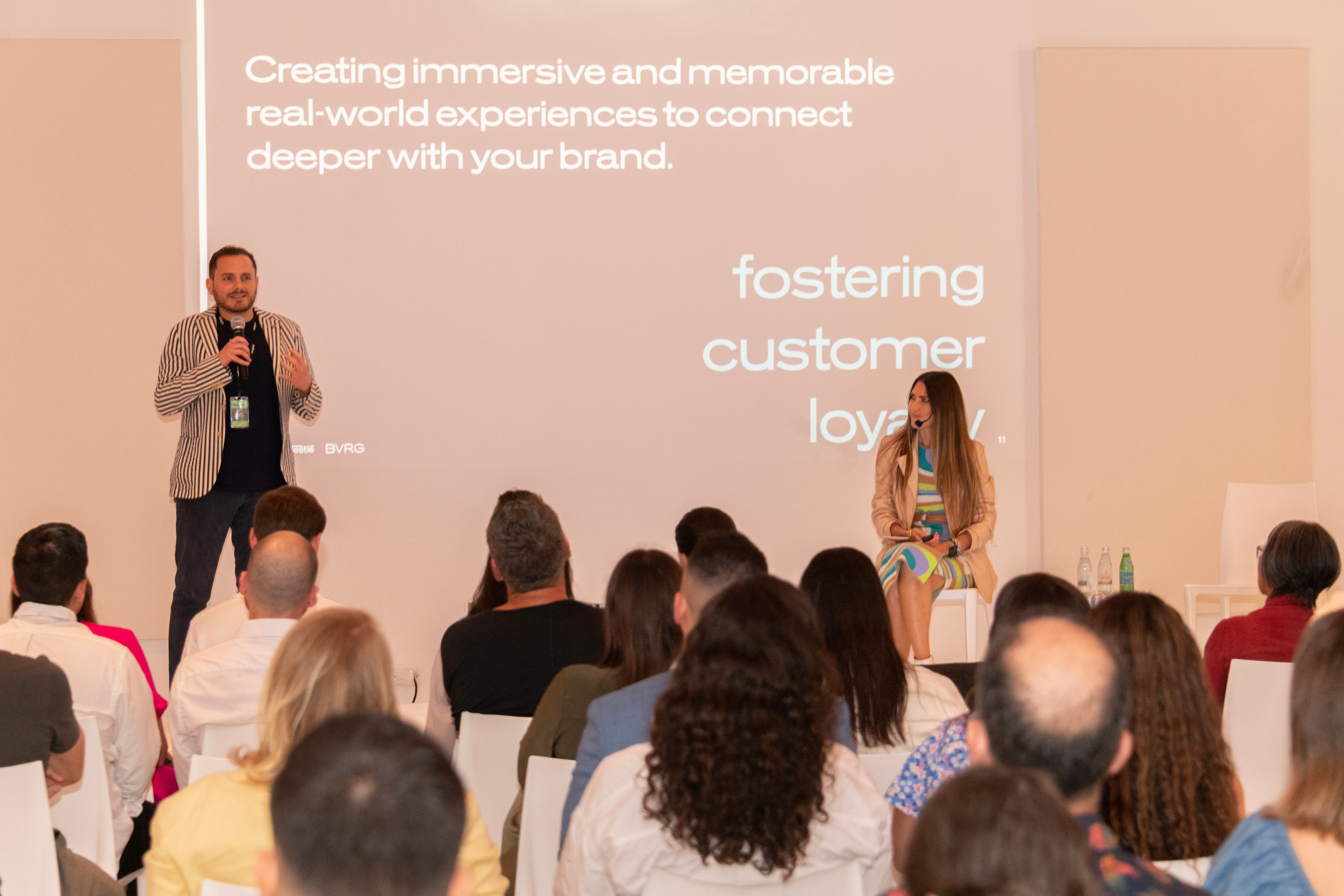 Speaker presenting on immersive brand experiences, with an audience seated and listening attentively.
