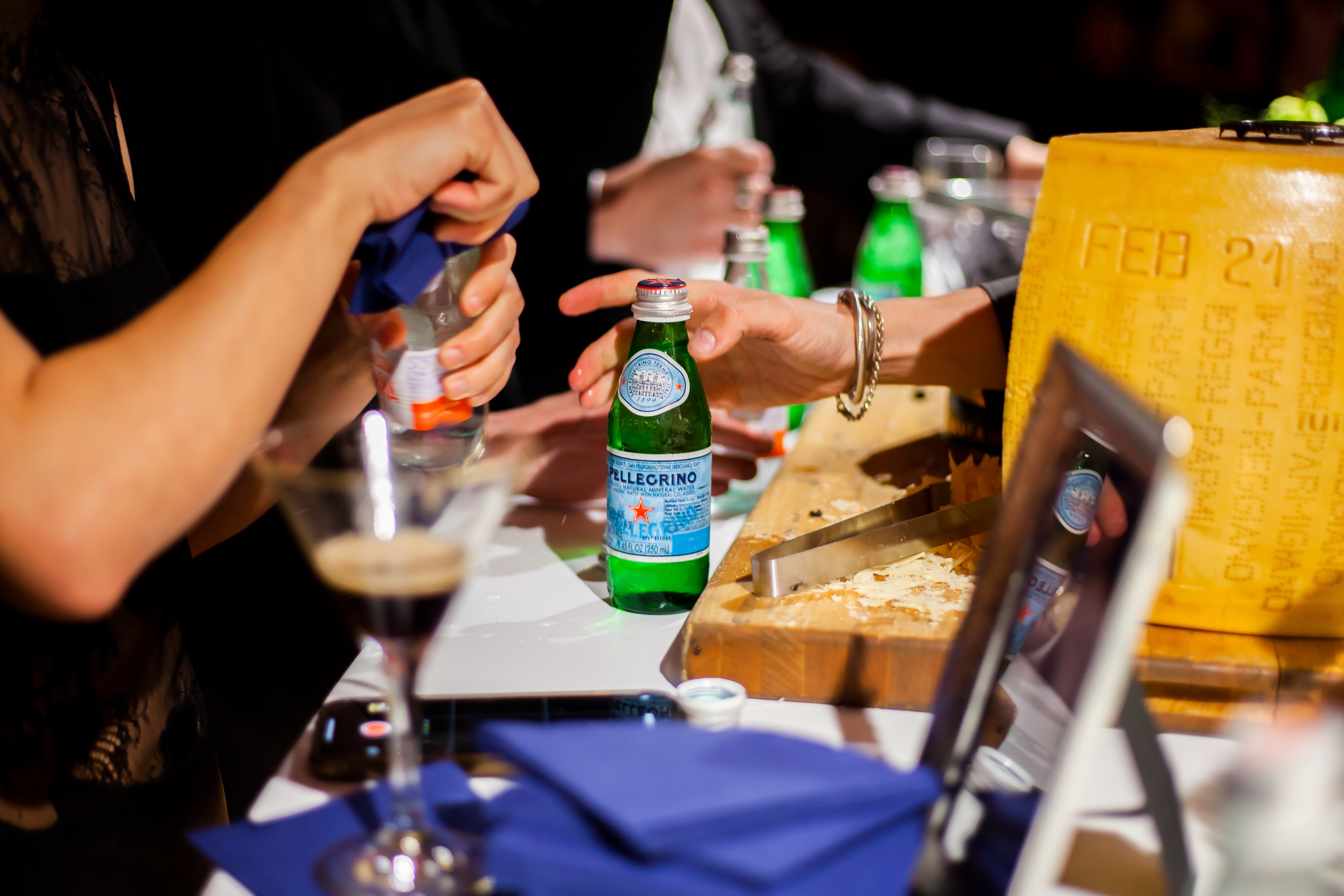 Bartenders serving bottles of Acqua Panna and S.Pellegrino next to a large cheese wheel.