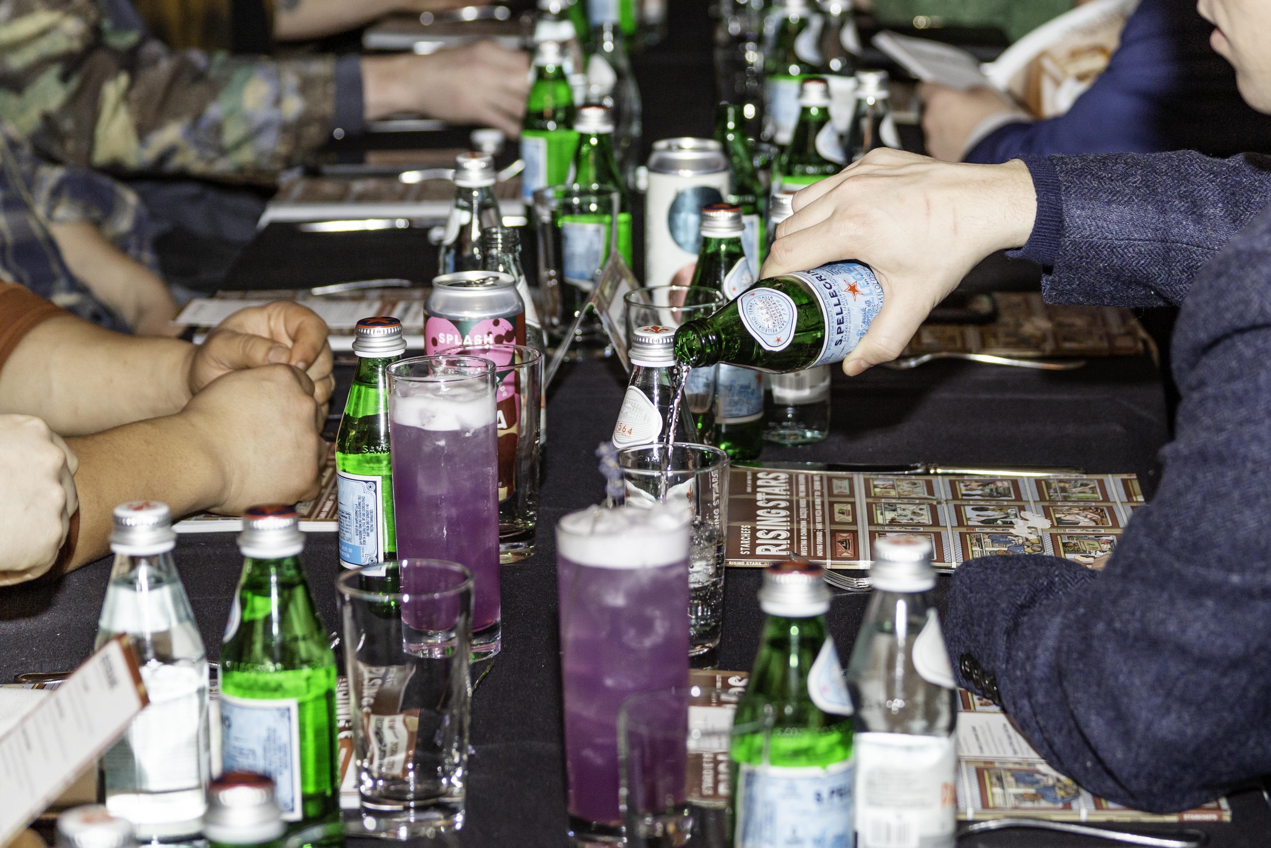 A person pouring S.Pellegrino into a glass at a Rising Stars event dinner.
