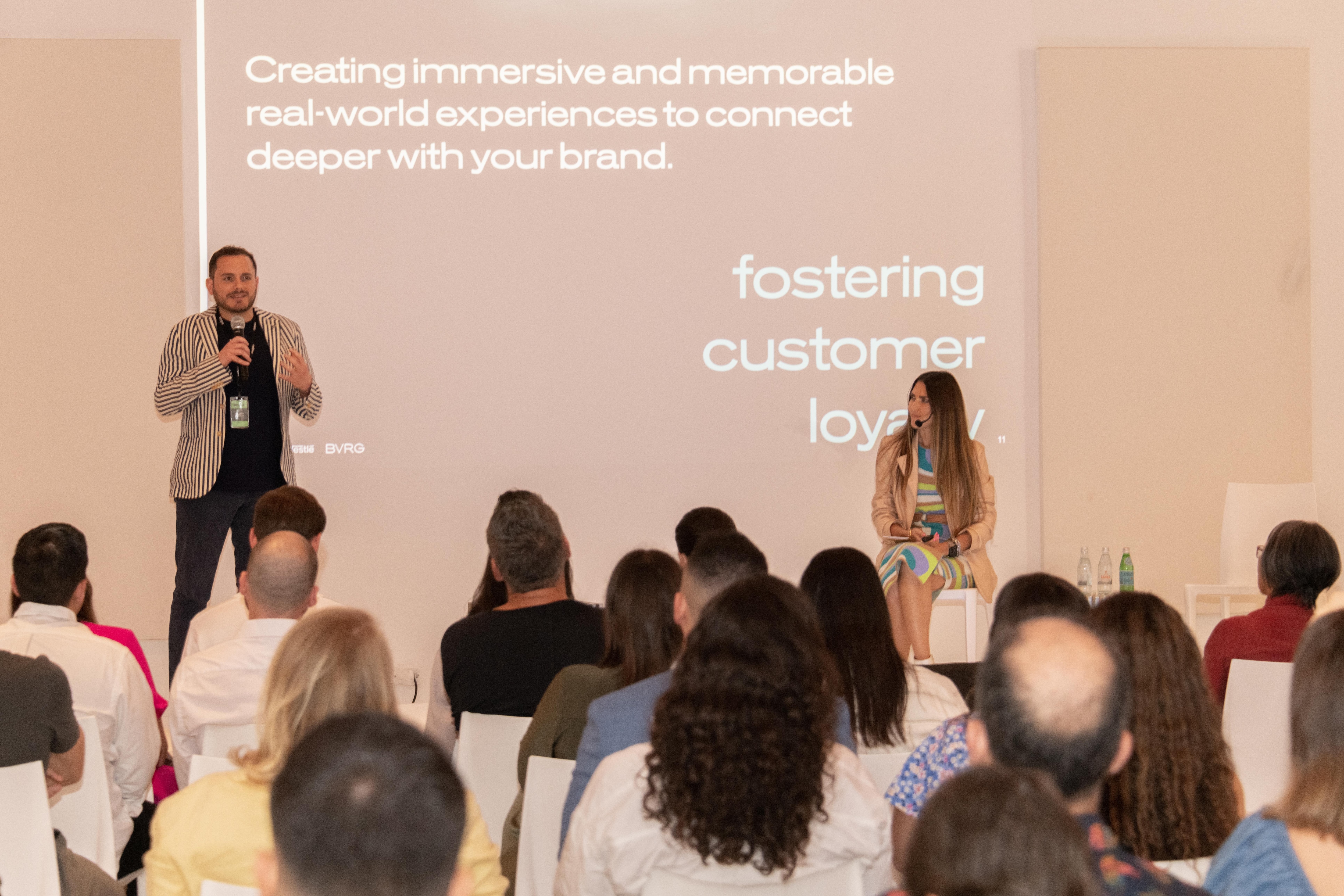 Speaker presenting on immersive brand experiences, with an audience seated and listening attentively.