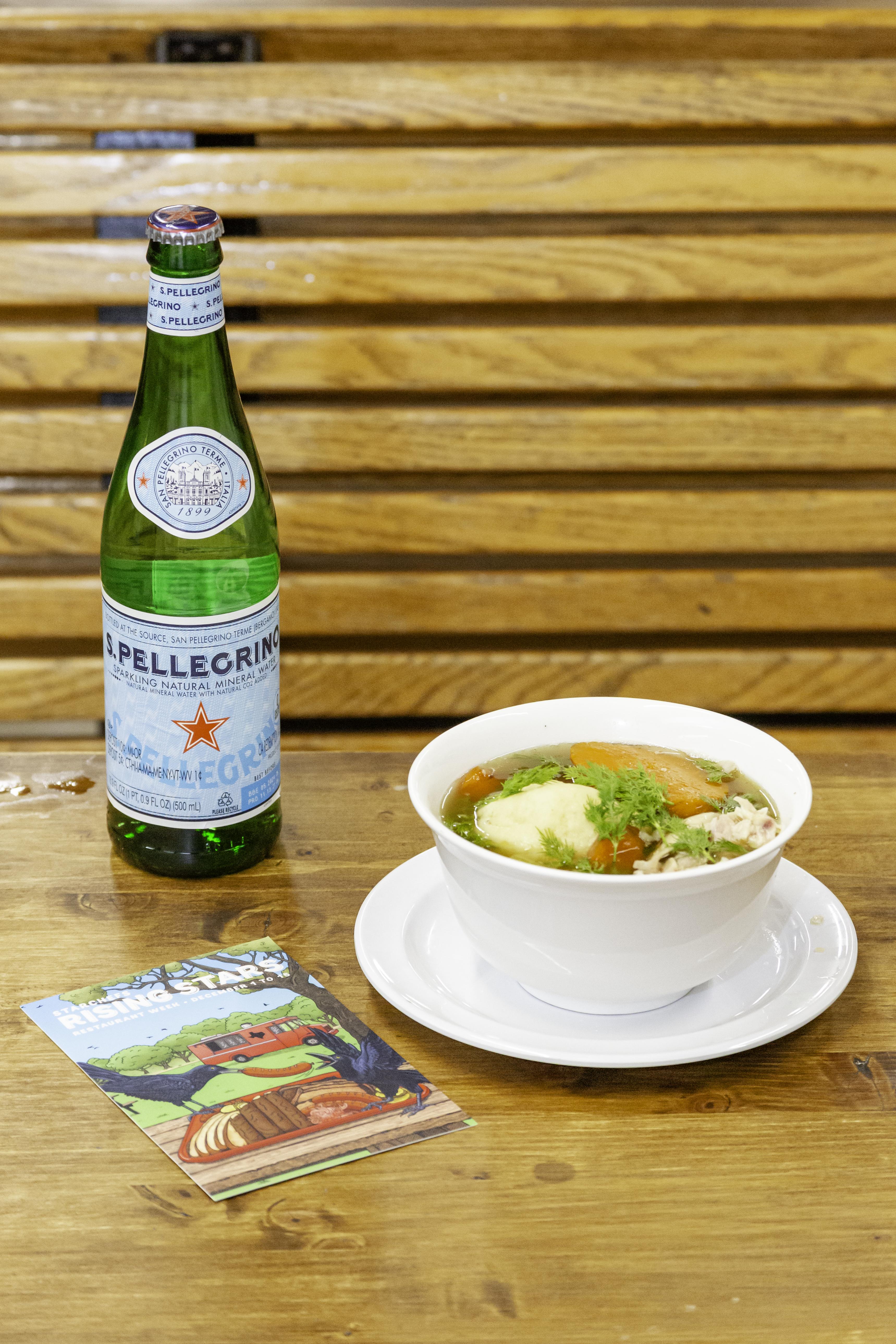 A bowl of soup with a bottle of S.Pellegrino on a table, part of the Rising Stars event.